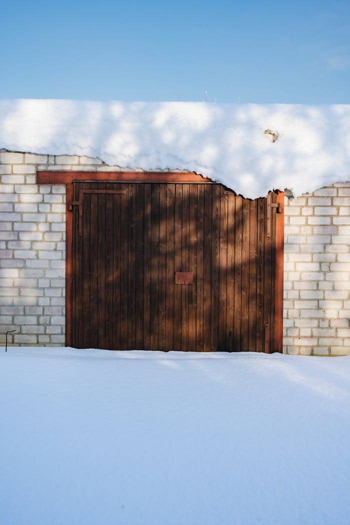 A wooden garage door framed by brick walls under a clear blue sky with fresh snow.