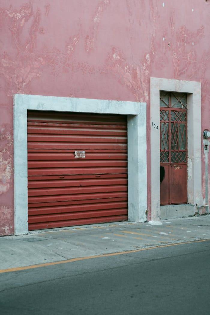 my-steps Close-up of a faded red garage and door on a pink wall in Aguascalientes, Mexico, showcasing urban decay.