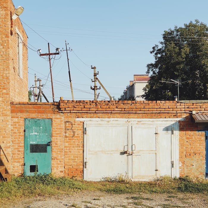 A rustic brick wall featuring a green door and white garage door under clear skies, casting distinct shadows.
