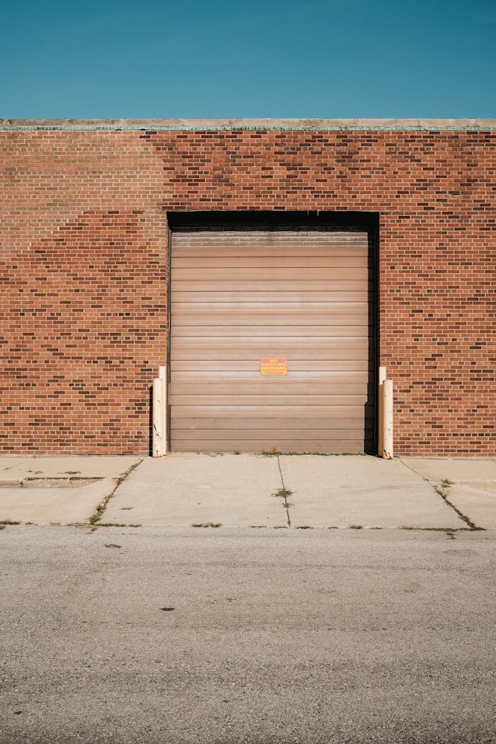 Brick industrial building featuring a closed metal garage door under bright sunlight.