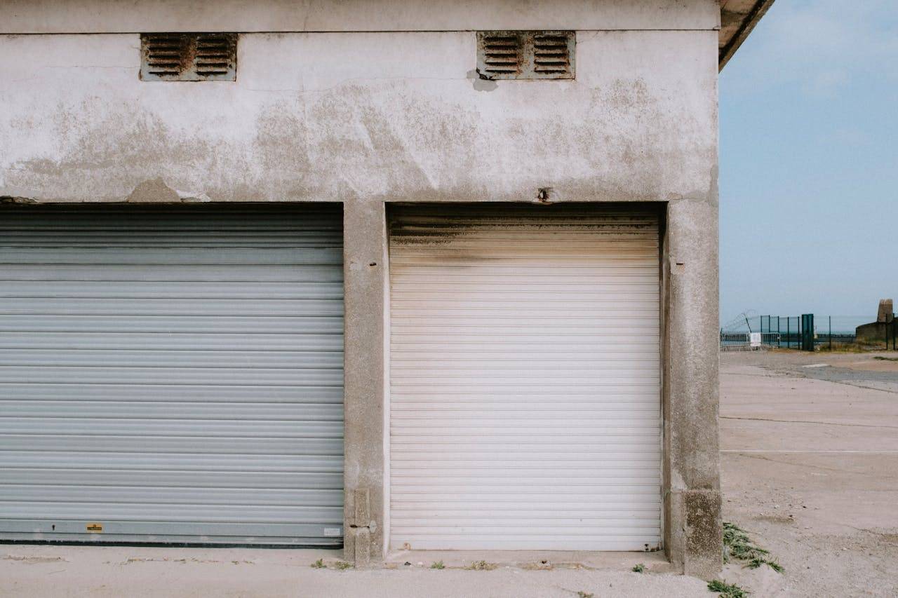 A detailed view of a weathered industrial building façade with rusty roll-up doors and a concrete exterior.