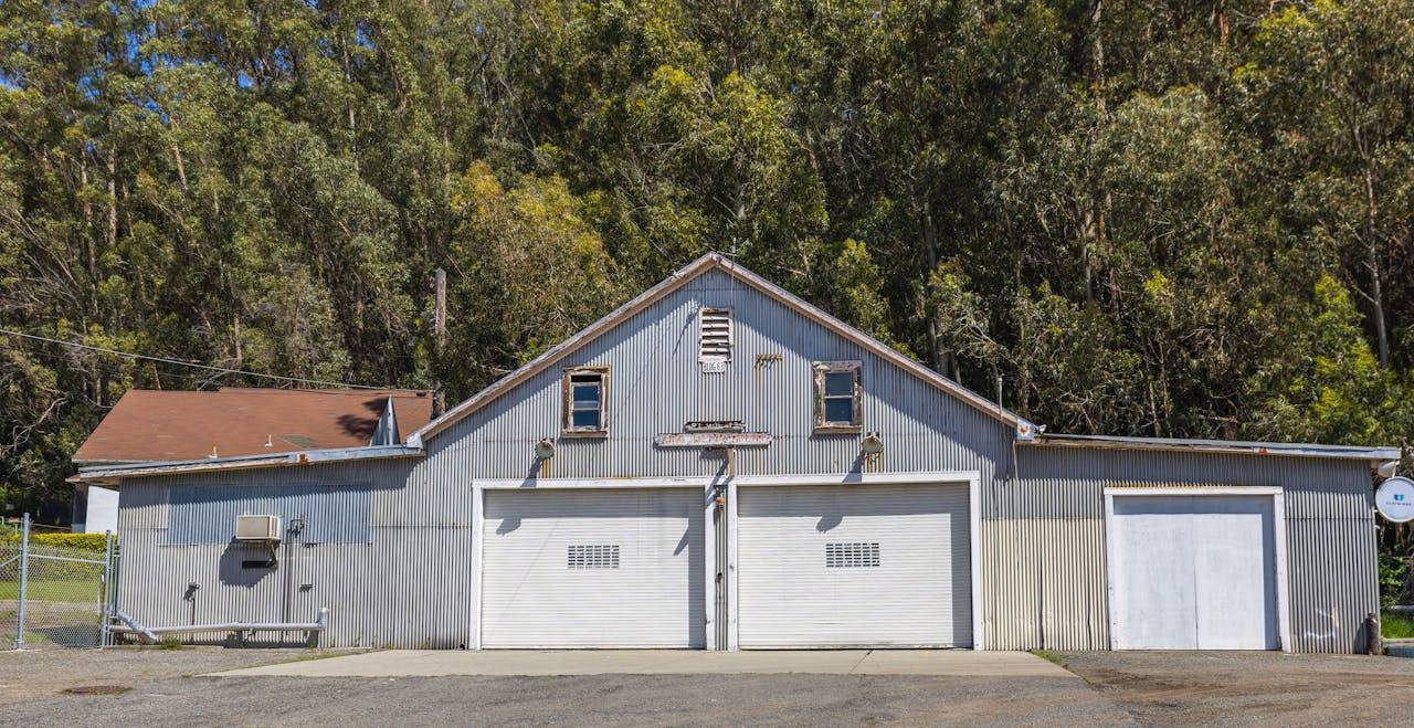 A rustic metal garage with a corrugated facade surrounded by dense trees.