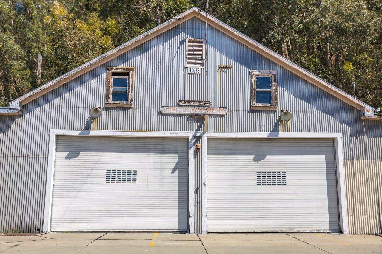 A sunlit vintage metal garage with double doors and rustic charm amidst trees.