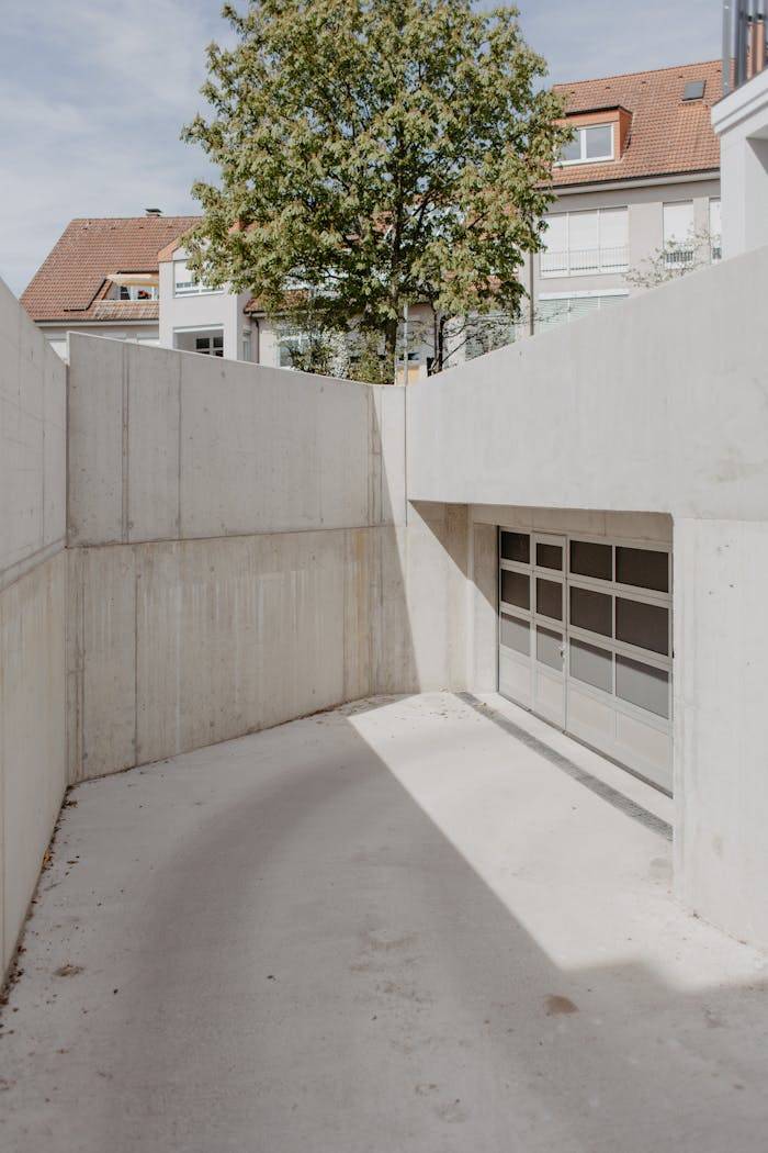 A minimalist concrete ramp leading to a modern underground garage entrance, surrounded by urban architecture.