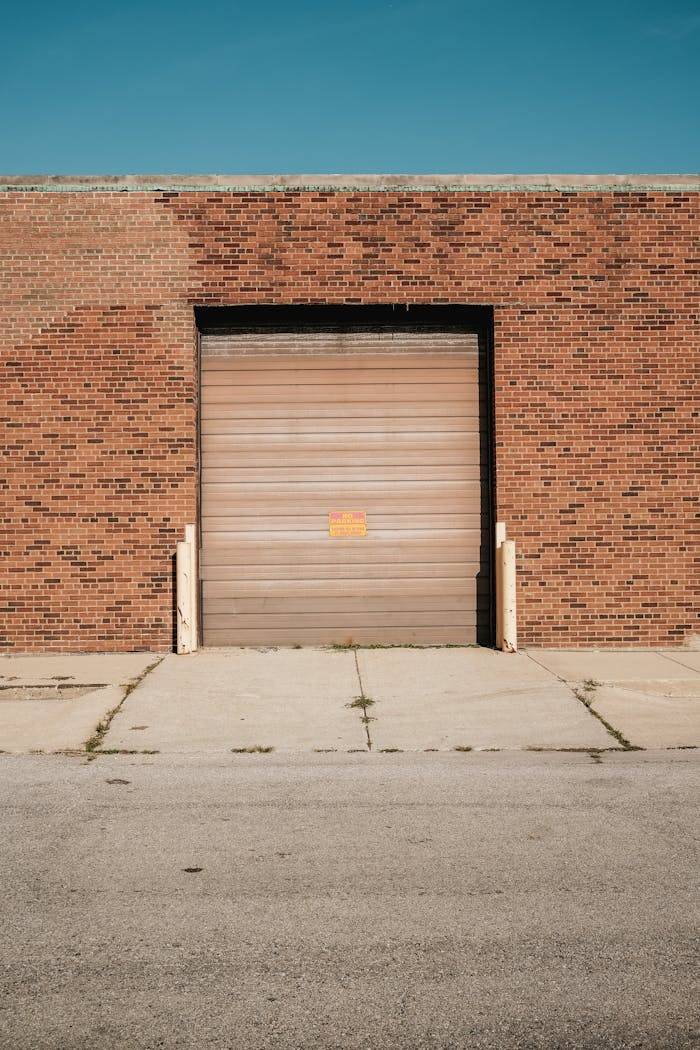 A brick warehouse with a closed roller door under a clear blue sky.