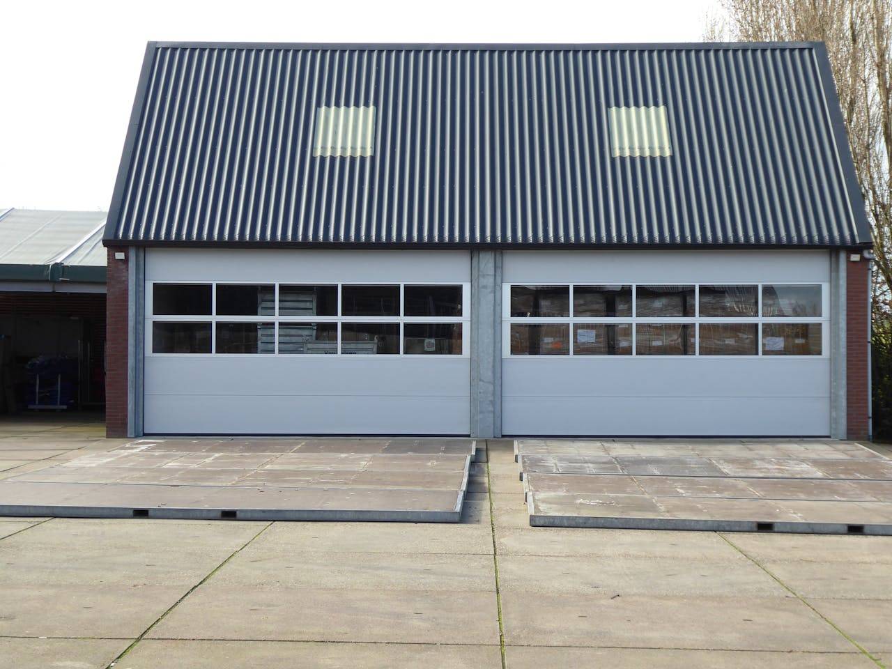 heros-img Front view of a modern warehouse building with corrugated roofing and skylights.