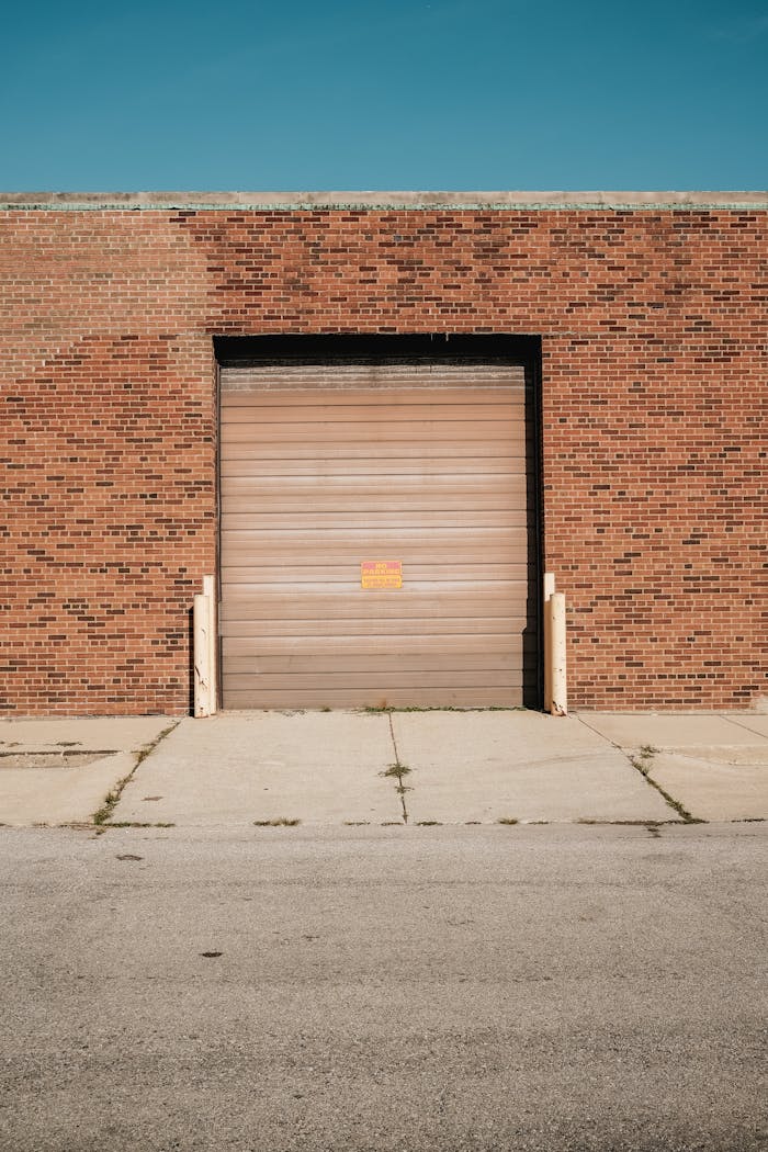 A brick warehouse with a closed roller door under a clear blue sky.