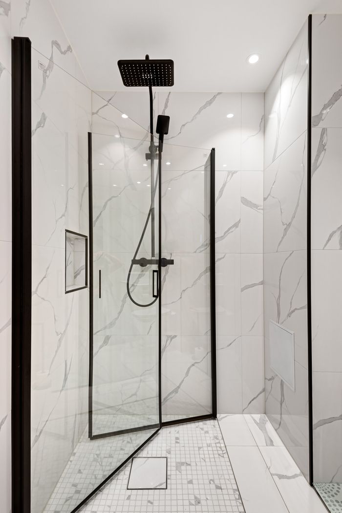 Elegant modern shower featuring sleek marble tiles and a glass door for a minimalist aesthetic.