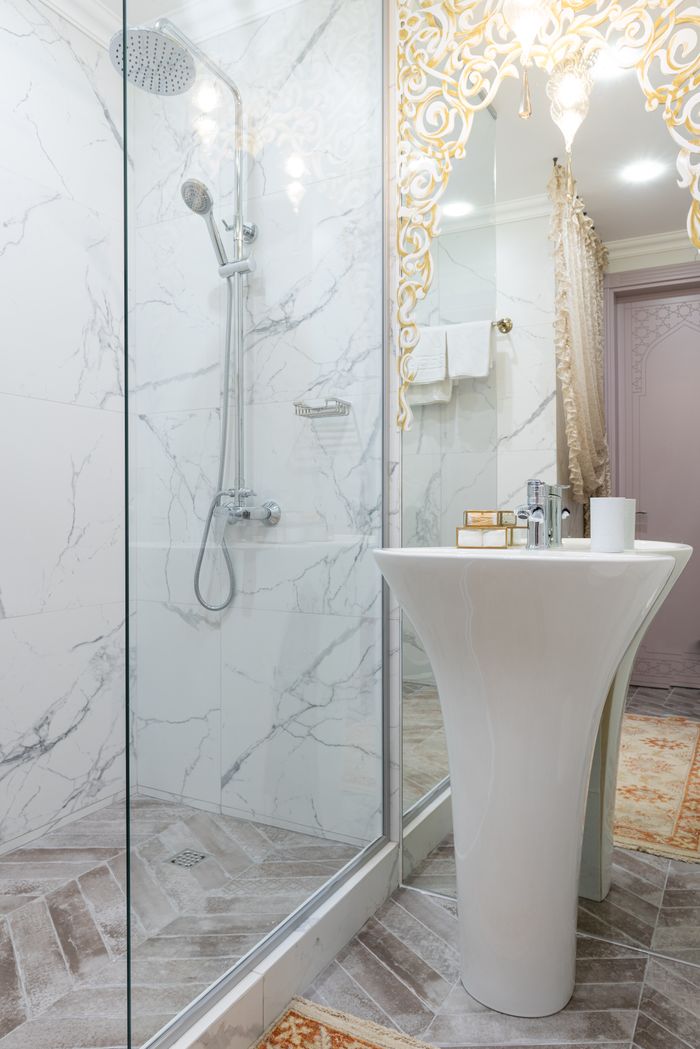 Interior of modern bathroom with transparent glass shower cabin near white sink placed near mirror with reflection of light room