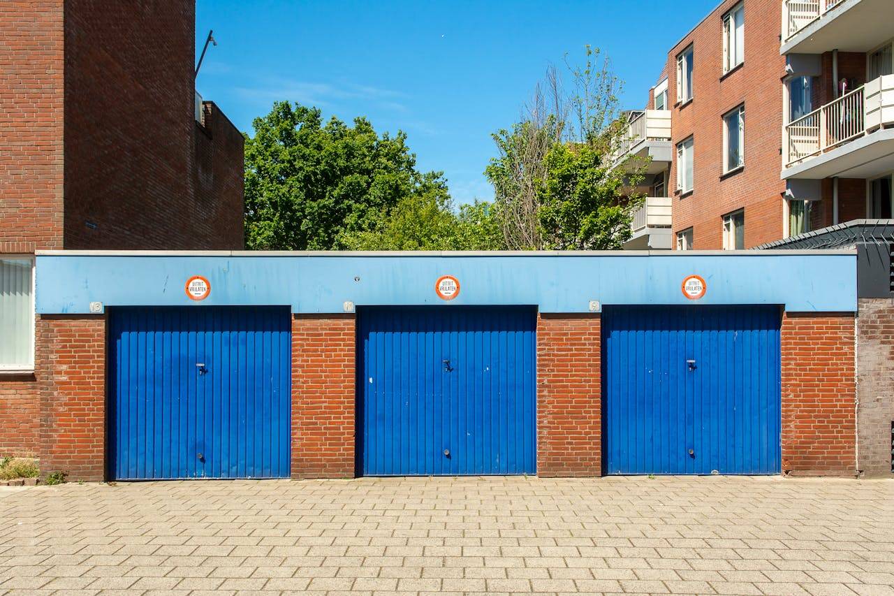 about-us-02 Three blue garage doors in a brick building on a sunny day.