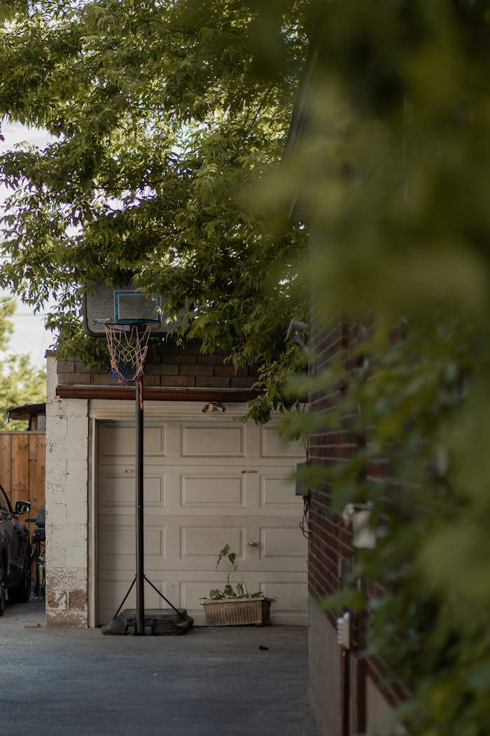 Serene backyard showing a basketball hoop near a garage, surrounded by lush greenery.