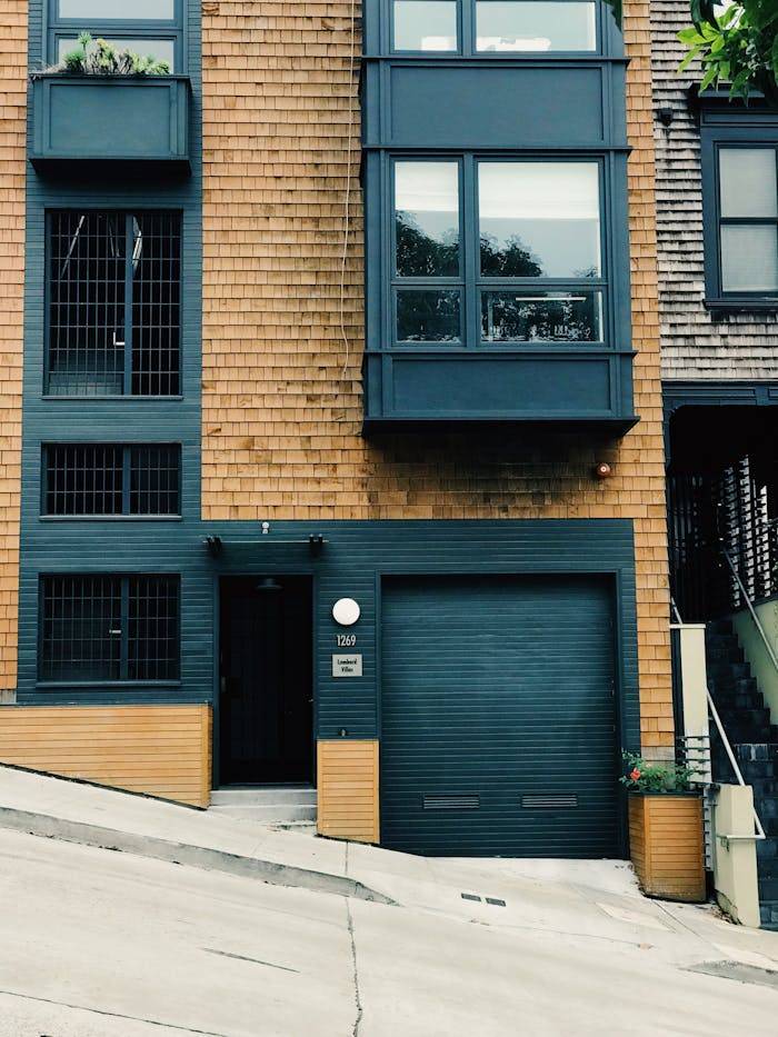 A modern residential building facade featuring a garage and sloping street in an urban setting.