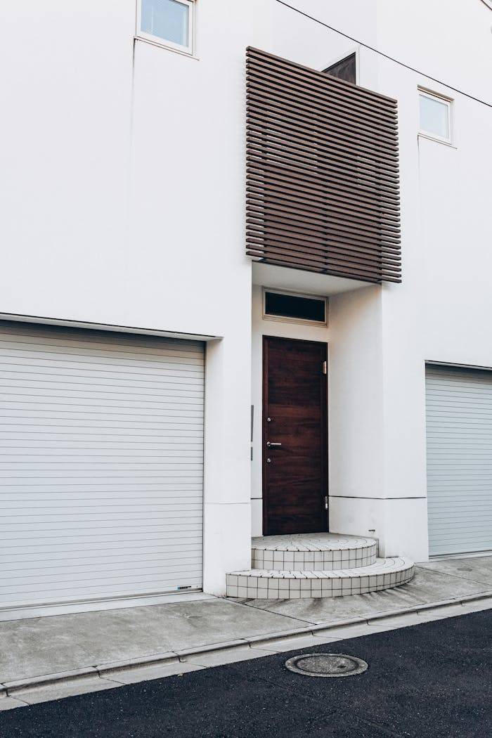Contemporary white building facade with wooden door and twin garage entrances.