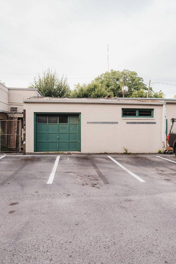 A small garage surrounded by trees and empty parking lot under a soft sky.