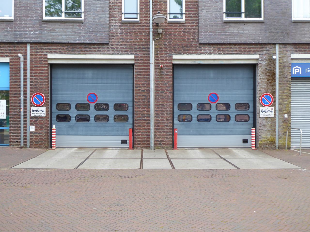 Closed industrial garage doors with no parking signs and brick facade.