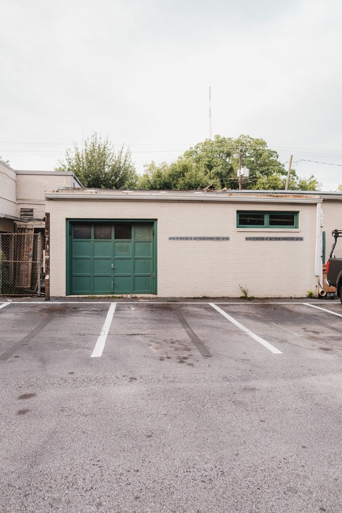 A small garage surrounded by trees and empty parking lot under a soft sky.
